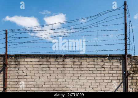 Vecchia prigione abbandonata, muro di mattoni bianchi con recinzione spinato in metallo arrugginito sullo sfondo Blue Sky Foto Stock