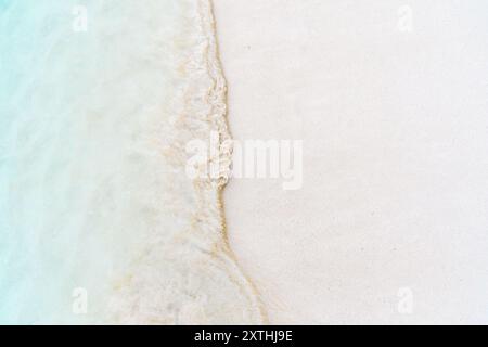 L'acqua blu turchese dell'oceano incontra la spiaggia di sabbia bianca. L'onda schiumosa lambisce dolcemente sulla riva, suggerendo tranquillità e relax. Vista aerea Foto Stock