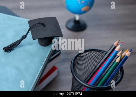 Cappuccio graduato sopra una pila di libri, un globo e una collezione di matite colorate. Concetto di istruzione e apprendimento. Foto Stock