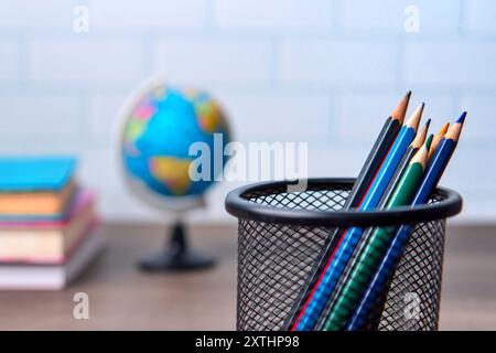 Un primo piano di un portamatite pieno di matite colorate, un globo e una pila di libri. Concetto di istruzione e conoscenza. Foto Stock