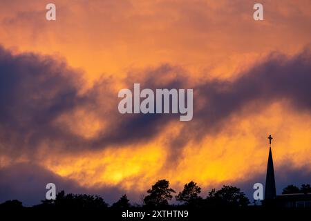 Sagoma di uno skyline al tramonto, con una guglia della chiesa e un incrocio contro un caldo cielo arancione. Foto Stock