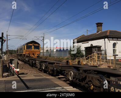 La locomotiva diesel GBRF n. 66742 passa sopra il passaggio a livello e attraverso il sito dell'ex stazione di Haughley nel Suffolk martedì 13.8.2024 Foto Stock