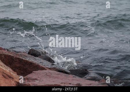 Primo piano dello spruzzo di una piccola onda che si schianta sulle rocce. Foto Stock