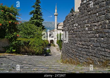 In primo piano, una robusta parete di mattoni si erge ferma, mentre sullo sfondo, un minareto alto ed elegante raggiunge il cielo, appartenente alla moschea di GJ Foto Stock