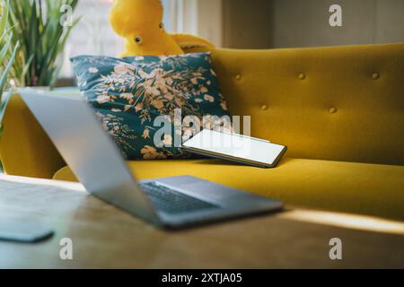Modello con schermo vuoto del tablet. Comodo divano interno. Aprire il computer portatile su un tavolo di legno. Piante verdi Foto Stock