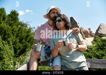 Una giovane coppia gay si diverte a fare un'escursione estiva insieme, fermandosi per ammirare il panorama e condividere un momento d'amore. Foto Stock