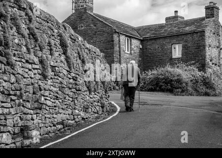 Un vecchio che cammina attraverso il villaggio di Muker, Swaledale, North Yorkshire Foto Stock