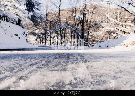 Visuale ad angolo basso su una strada asfaltata ricoperta di neve che conduce a una svolta a sinistra. Alberi sullo sfondo. Diminuire la prospettiva. Messa a fuoco selettiva. Foto Stock