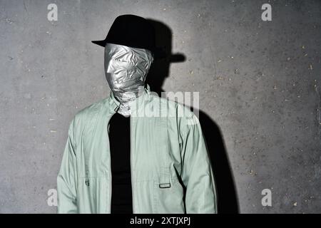 Uomo misterioso in cappello con nastro adesivo per il viso su sfondo grigio. Horror, segreto e concetto in incognito Foto Stock