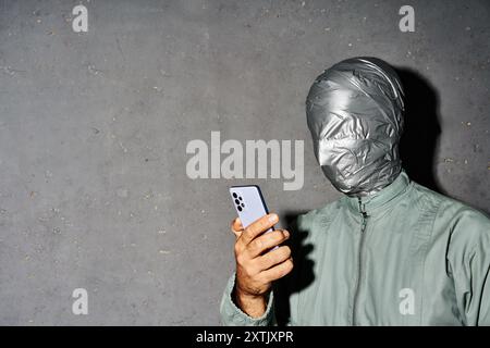 Misterioso uomo con nastro adesivo, messaggi di testo sul telefono cellulare, ama le comunicazioni online su sfondo grigio Foto Stock