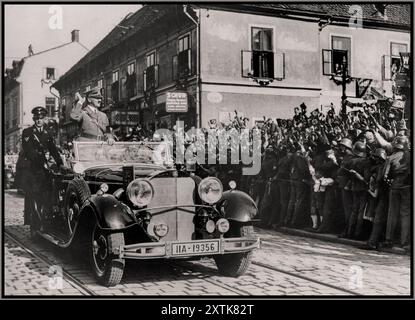 ANSCHLUSS Adolf Hitler in piedi sulla sua Mercedes aperta, saluta le folle di entusiasti austriaci che salutano sventolando le bandiere di Swastika dopo l'annessione / Anschluss noto anche come Anschluß Österreichs l'annessione dello Stato federale d'Austria al Reich tedesco il 13 marzo 1938. Foto Stock