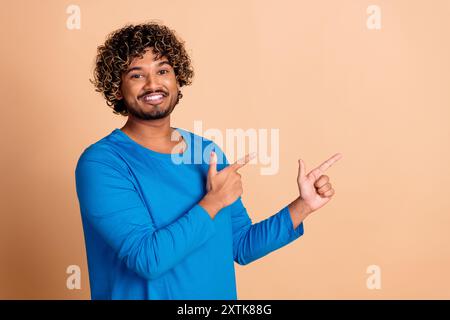 Foto di un uomo allegro che indossa abiti blu alla moda che mostrano uno spazio vuoto isolato su sfondo di colore beige Foto Stock