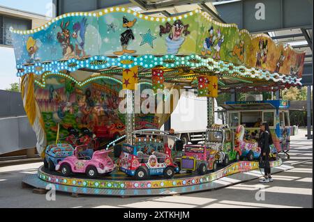 Viladecasn, SPAGNA - 15 AGOSTO 2024: Giostra fieristica con auto e aerei per bambini illuminata sotto un cielo azzurro, perfetta per il divertimento in famiglia. Foto Stock