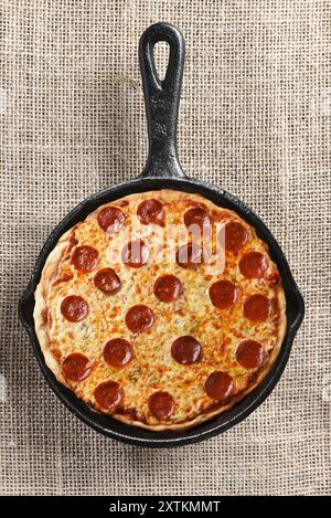 Spillatura ad angolo alto di formaggio e pizza al peperoni in una padella di ghisa. Foto Stock