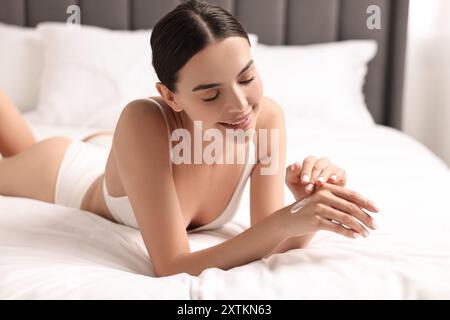 Donna sorridente che applica la crema sulla mano sul letto. Cura del corpo Foto Stock