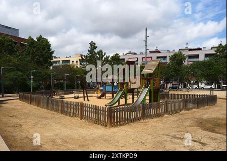 Area giochi esterna con attrezzature ricreative, recintata da recinzione in legno, con alberi ed edifici sullo sfondo. Foto Stock