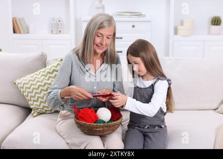 Nonna sorridente che insegna a sua nipote a lavorare a maglia sul divano a casa Foto Stock