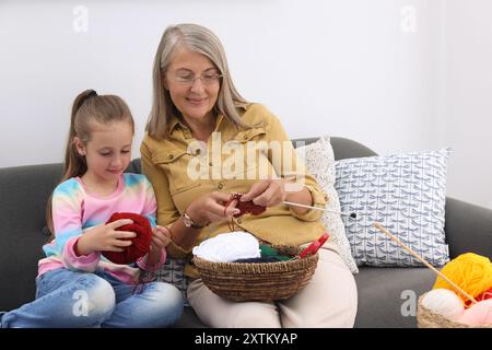 Nonna che insegna a sua nipote a lavorare a maglia sul divano a casa Foto Stock