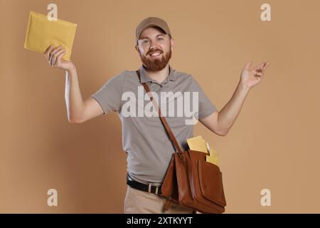Felice giovane postino con borsa in pelle che consegna lettere su sfondo marrone Foto Stock