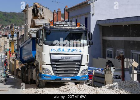 Nancy, Francia - Vista su un veicolo DAF XF 510 bianco con semirimorchio ribaltabile blu caricato da un escavatore cingolato in un cantiere. Foto Stock