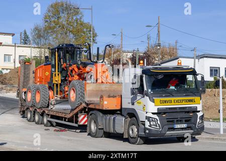 Saint-Max, Francia - Vista su un autocarro da trasporto pesante Volvo FMX 500 con motorgrader CAT 140M3 parcheggiato in cantiere. Foto Stock