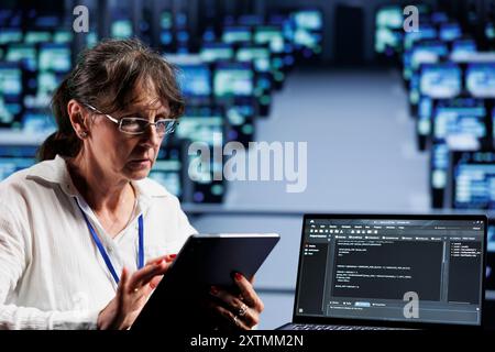 Vecchio informatico che scrive codice script nel data center su un terminale portatile. Professionisti esperti che eseguono lavori di manutenzione nella sala server, aggiornando il software dei sistemi di perforazione per prevenire i malfunzionamenti Foto Stock
