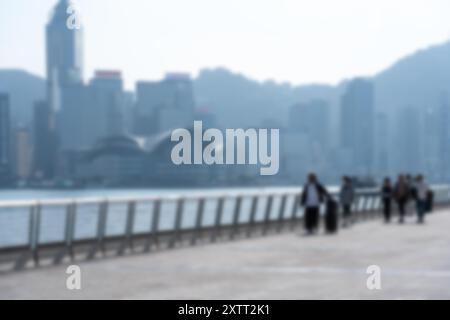 Un'immagine sfocata di persone che camminano su un lungomare di fronte a un grande skyline della città. Foto Stock