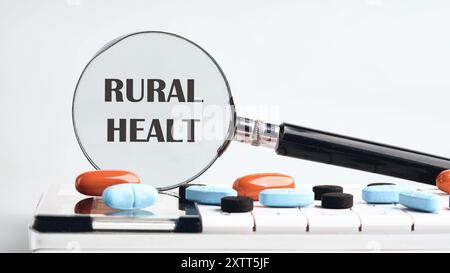 Concetto medico. PAROLE DI RURAL HEALT scritte attraverso una lente d'ingrandimento su una calcolatrice con tavolette su sfondo grigio. Il concetto di medicina Foto Stock