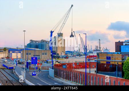 Tarragona, Spagna - 15 luglio 2024: Zona portuale affollata con gru e silos, con attività di movimentazione merci e navi attraccate su una colorazione Foto Stock