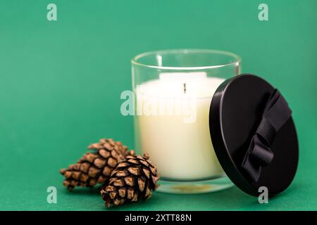 Candela su sfondo verde e coni di pino naturali, aroma di foresta e aghi di pino, aroma di Natale e Capodanno Foto Stock