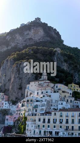 Questa foto cattura l'architettura mozzafiato degli edifici collinari di Amalfi, annidati contro le torreggianti scogliere e la vegetazione lussureggiante, che mettono in mostra Foto Stock