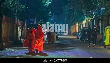 Nuova Delhi, Delhi, India. Donne che indossano abiti tradizionali saris che camminano sulla strada notturna. Foto Stock