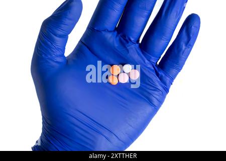 Medico che indossa guanti blu con pillole multicolore nel palmo su sfondo bianco. Vista dall'alto Foto Stock