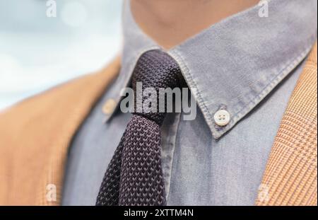 Uomo anonimo vestito con un elegante abbigliamento casual dallo sfondo blu. L'outfit presenta una giacca beige con camicia blu e cravatta in maglia. Foto Stock