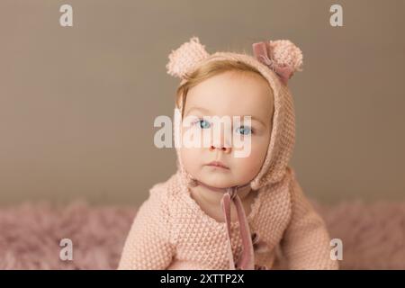 Vista frontale di una bambina dagli occhi blu con cofano e romper rosa Foto Stock