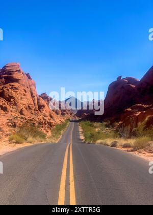 Lunga strada che taglia le formazioni di roccia rossa sotto un cielo azzurro Foto Stock