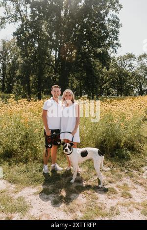 Giovane coppia con un cane in piedi davanti ai fiori selvatici Foto Stock