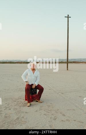 Uomo in un cappello da cowboy seduto su una cassa in un vasto deserto aperto Foto Stock