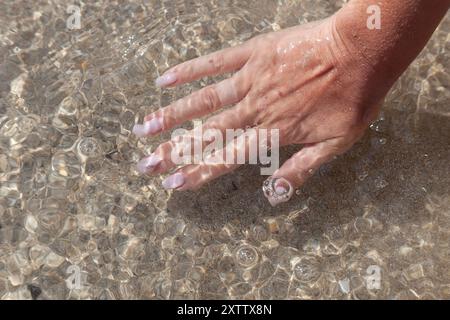 Mani con acqua pura. Primo piano della mano di una donna che tocca l'acqua del mare. La mano di una persona che si allontana per toccare una superficie d'acqua increspata, esplorando il Foto Stock