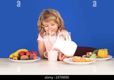 Capretto che versa latte intero di mucche. Ritratto di bambino mangiare cibo fresco sano in cucina a casa. Bambino che mangia la colazione prima della scuola. Foto Stock