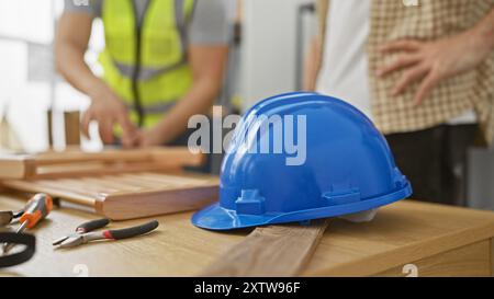 Due uomini che lavorano insieme in un'officina di falegnameria con attrezzi e un elmetto blu su un tavolo di legno. Foto Stock