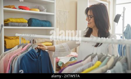 Donna sorridente che sfoggia abiti in un guardaroba moderno e luminoso. Foto Stock