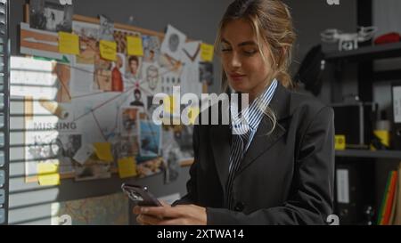 Una donna bionda concentrata nell'ufficio di un detective esamina il suo smartphone vicino a una commissione investigativa. Foto Stock