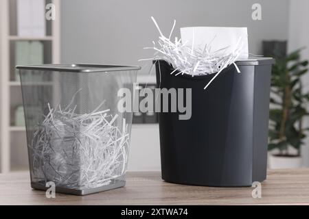 Distruggendo fogli con trituratore e strisce di carta in un cestino di metallo su un tavolo di legno in ufficio Foto Stock