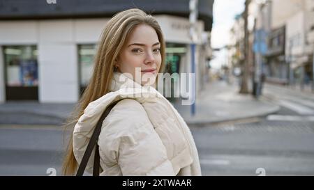 Una giovane donna informale, attraente e dai capelli biondi che cammina in una strada della città alla luce del giorno, trasuda fascino urbano. Foto Stock