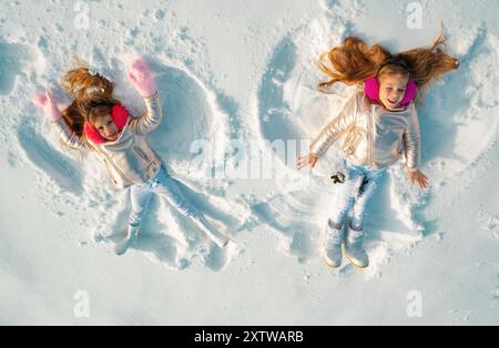 Angeli di neve fatti da bambini nella neve. Bambini sorridenti sdraiati sulla neve con spazio fotocopie. Bambini divertenti che fanno l'angelo della neve. Vista dall'alto. Foto Stock