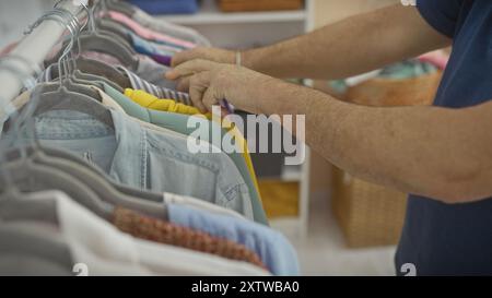 Un uomo sfoglia vari vestiti su appendiabiti in un armadio interno ben organizzato. Foto Stock