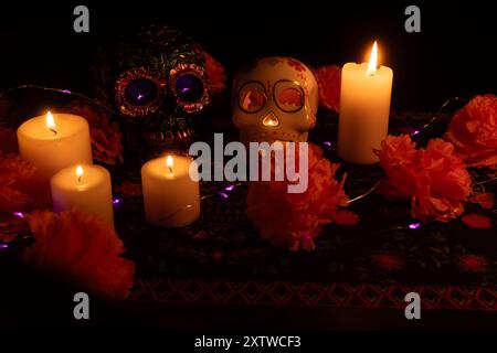 Un'affascinante scena di Día de los Muertos con due teschi. Uno decorato con fiori metallici e l'altro con una candela all'interno, circondato da mari Foto Stock
