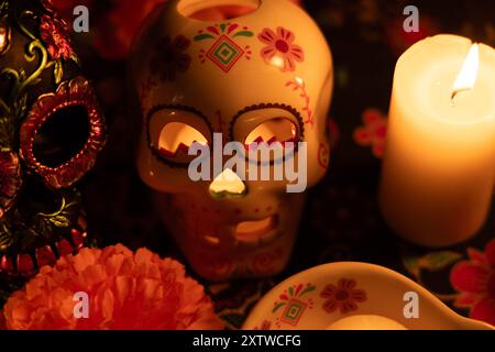 Un primo piano di due teschi: Uno con fiori metallici e l'altro con una candela che si illumina all'interno. Marigolds e candele accese completano il giorno dei morti Foto Stock