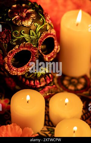 Una vista dall'alto verso il basso di un cranio adornato con fiori di metallo, circondato da calendule arancioni e candele accese. Tutti gli oggetti sono collocati su un clo Día de los Muertos Foto Stock